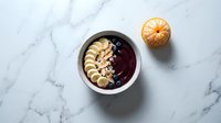 Acai bowl with sliced banana and granola on marble surface, overhead view. Healthy breakfast and smoothie bowl concept for food and wellness design.