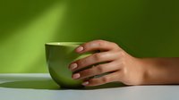 Female hands with manicured nails holding green ceramic cup on green background with soft shadows and minimalist composition, wellness and mindfulness concept.