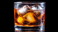 Glass of whiskey with ice cubes on black background, amber liquid with bubbles and condensation drops, alcoholic beverage for bar and restaurant concepts.