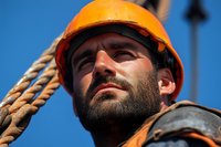 Construction worker in orange hard hat looking up with rope and blue sky background for industrial safety and building projects.