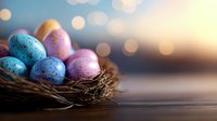 Colorful speckled Easter eggs in blue and pink resting in natural twigs nest against blurred bokeh background, creating festive spring holiday atmosphere.