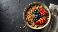 Granola bowl with fresh berries and sliced strawberries on dark slate surface, overhead view for breakfast, healthy eating, and nutrition content.