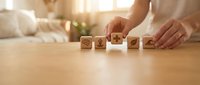 Person arranging wooden blocks with eco-friendly symbols on table in bright modern living room for sustainable lifestyle concept.
