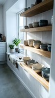 Wooden floating shelves display ceramic bowls and pottery in bright kitchen with white shiplap walls and large window, perfect for home decor and interior design projects.