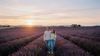 Couple standing in blooming lavender field at sunset, holding hands in romantic countryside landscape with golden hour lighting.