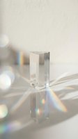 Clear crystal prism refracting light into rainbow spectrum on white surface with bokeh background. Optical physics demonstration.
