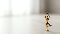 Golden brass figurine in tree yoga pose on white surface with soft blurred background for meditation wellness and mindfulness concepts.