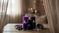 Purple and black candles burning with warm flames creating cozy atmosphere on wooden table with pinecones for home decor and relaxation.