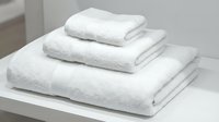 Stack of three fluffy white cotton towels neatly folded on a shelf, conveying cleanliness, luxury, and spa comfort for hotel or home use.