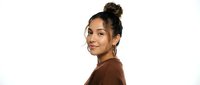 Young Hispanic woman with curly hair in bun smiling confidently in brown sweater on white background isolated for design and marketing materials.