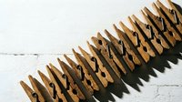 Row of wooden clothespins arranged in line on white wooden surface creating organized pattern with natural shadows for laundry and household concepts.