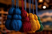 Colorful yarn tassels hanging in row showing blue, red, yellow and green wool decorative elements against blurred warm background. Macro craft photography.