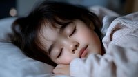 Young Asian girl sleeping peacefully in bed with soft natural lighting creating gentle shadows on face. Cozy bedroom scene shows innocence and tranquility.