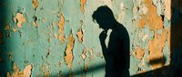 Silhouette of a person in contemplative pose against weathered turquoise and orange peeling wall with dramatic shadow, conveying melancholy, isolation, and introspection for editorial and conceptual projects.