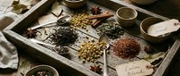 Vintage wooden tray filled with aromatic spices, herbs and tea blends with handwritten labels for culinary and wellness applications.