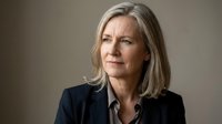 Professional mature Caucasian businesswoman with blonde hair in dark suit looking confident and determined against neutral background for corporate use.