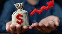 Money bag with dollar sign and rising red arrow floating above male hands against dark background, representing financial growth and investment success.