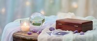 Spiritual meditation setup with crystal ball, wooden box, amethyst stones and candle on white fabric for wellness and mindfulness practices.