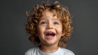 Joyful Caucasian toddler with curly blonde hair and bright smile laughing against dark background, expressing pure happiness and genuine emotion in studio portrait.