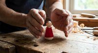 Craftsman hands protecting small wooden figure on workbench in workshop. Handmade toy creation, woodworking artisan craft, safety and care concept for handcrafted items.