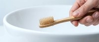 Hand holding eco-friendly bamboo toothbrush over white ceramic sink, sustainable oral care and zero waste bathroom routine concept.