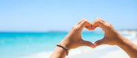 Hands forming heart shape against turquoise ocean and blue sky background. Summer vacation love concept for romantic travel and beach holiday destinations.