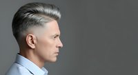 Young man with short, styled silver-gray hair and fade haircut wearing light blue shirt in profile view against neutral background for grooming and barbershop concepts.