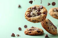 Chocolate chip cookies falling with chocolate pieces on mint green background for bakery advertising and food photography projects.