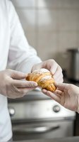 Professional baker in white uniform presenting fresh golden croissant with powdered sugar in modern commercial kitchen for culinary business marketing.