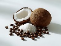 Fresh coconut cut in half with white flesh, whole coconut, shredded coconut flakes and coffee beans arranged on white surface for food photography.