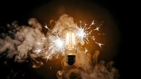 Glowing light bulb with electric sparks surrounded by dramatic smoke clouds against dark background symbolizing innovation and creative ideas.