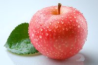 Fresh red apple with water droplets and green leaf on white surface, showcasing natural freshness for food and health concepts.