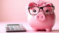 Pink ceramic piggy bank wearing black-rimmed glasses next to calculator on pink background, representing smart financial planning and budgeting concepts.