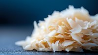 Fresh white coconut flakes scattered on dark background with selective focus and shallow depth of field, raw organic food ingredient for cooking and baking.