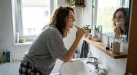 Young woman brushing teeth in modern bathroom mirror reflection morning routine dental hygiene self care healthy lifestyle daily habits wellness.
