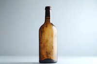 Vintage amber glass bottle photographed against light background, showing age marks and patina. Minimalist composition highlights nostalgic character and artisanal craftsmanship.