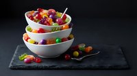 Colorful assorted jelly beans and gummy candies in stacked white bowls on dark slate board with vintage spoon for sweet treats and confectionery displays.