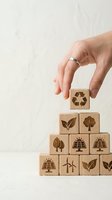 Hand placing wooden cube with recycling symbol on pyramid of eco-friendly blocks featuring renewable energy and nature icons for sustainable business concepts.