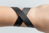 Two arms with light skin tone connected by black elastic band in X shape on white background, representing unity, support, teamwork, and connection for healthcare, fitness, and awareness campaigns.