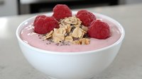 Pink raspberry yogurt smoothie bowl topped with fresh red raspberries, crunchy almond flakes and chia seeds in white ceramic bowl, healthy breakfast concept.