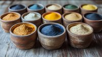 Vibrant natural powder pigments in rustic clay bowls arranged on wooden surface, featuring yellow, blue, white and orange organic dyes for textile and art projects.