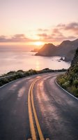 Winding coastal road with yellow center lines curves toward dramatic sunset over ocean and rocky islands, perfect for travel and adventure themes.