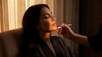 Professional makeup artist applying lipstick to young woman client in beauty salon with warm natural lighting for cosmetic treatment session.