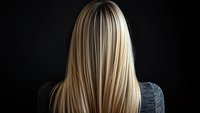 Straight blonde hair from behind on dark background showing woman with long smooth healthy hairstyle wearing casual grey top.