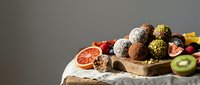 Assorted healthy energy balls with nuts seeds and dried fruits on wooden board with fresh berries and citrus slices for nutritious snacking and wellness.