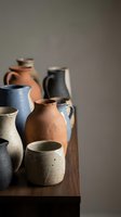 Handmade ceramic vessels in earthy tones arranged on wooden surface. Collection includes pitchers, jugs, and cups with natural glazes. Suitable for home decor, artisan product showcases, and lifestyle content.
