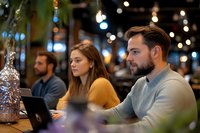 Young diverse team working late at cafe with laptops, focused on digital project. Casual business meeting in modern coffee shop with bokeh lights.