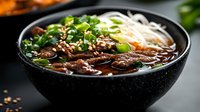 Asian beef noodle soup with tender meat slices, fresh herbs and rice noodles in rich dark broth served in black ceramic bowl for restaurant menu design.