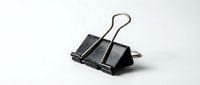 Black metal binder clip with silver wire handles isolated on white background for office supplies and stationery design projects.