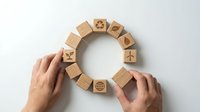 Hands arranging wooden blocks with business icons in circular formation on white background for corporate strategy and planning concepts.